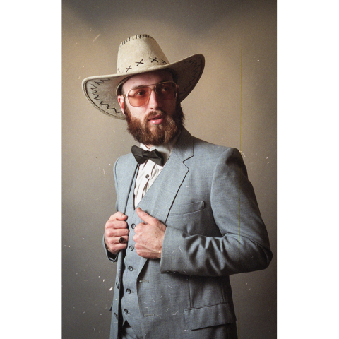 L'artiste avec un chapeau de cowboy sur la tête et portant une veste grise avec un noeud papillon.