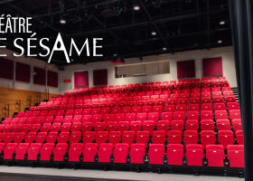Salle vide du Théâtre Le Sésame avec des sièges rouges en gradins, vue depuis la scène avec le logo en haut à gauche