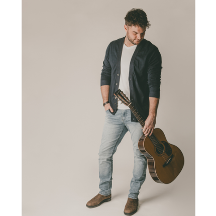 L'artiste Benny Jones debout avec sa guitare en main et la tête penché sur le côté